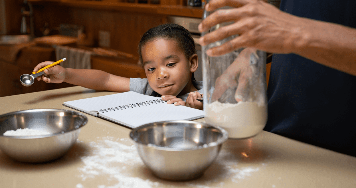 Child and adult baking, with flour, bowls, and a measuring spoon on a counter.