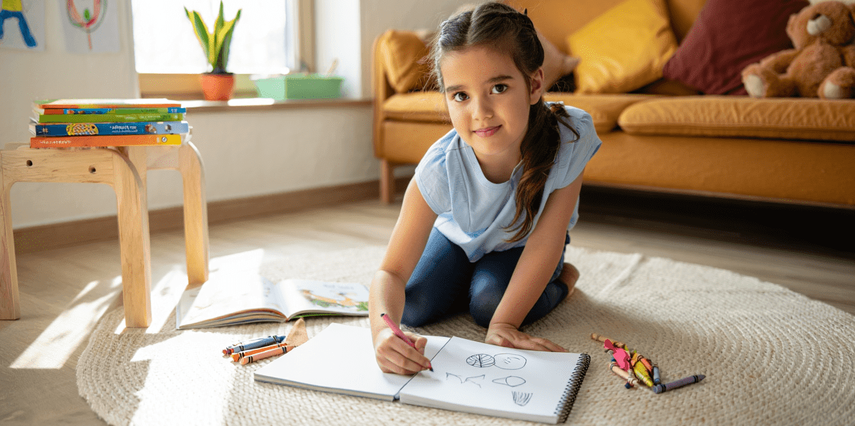 Child drawing in a sketchbook on the floor with crayons.