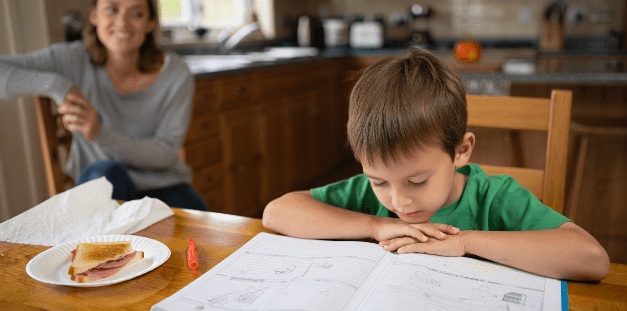 Child studying at a table with an adult nearby.