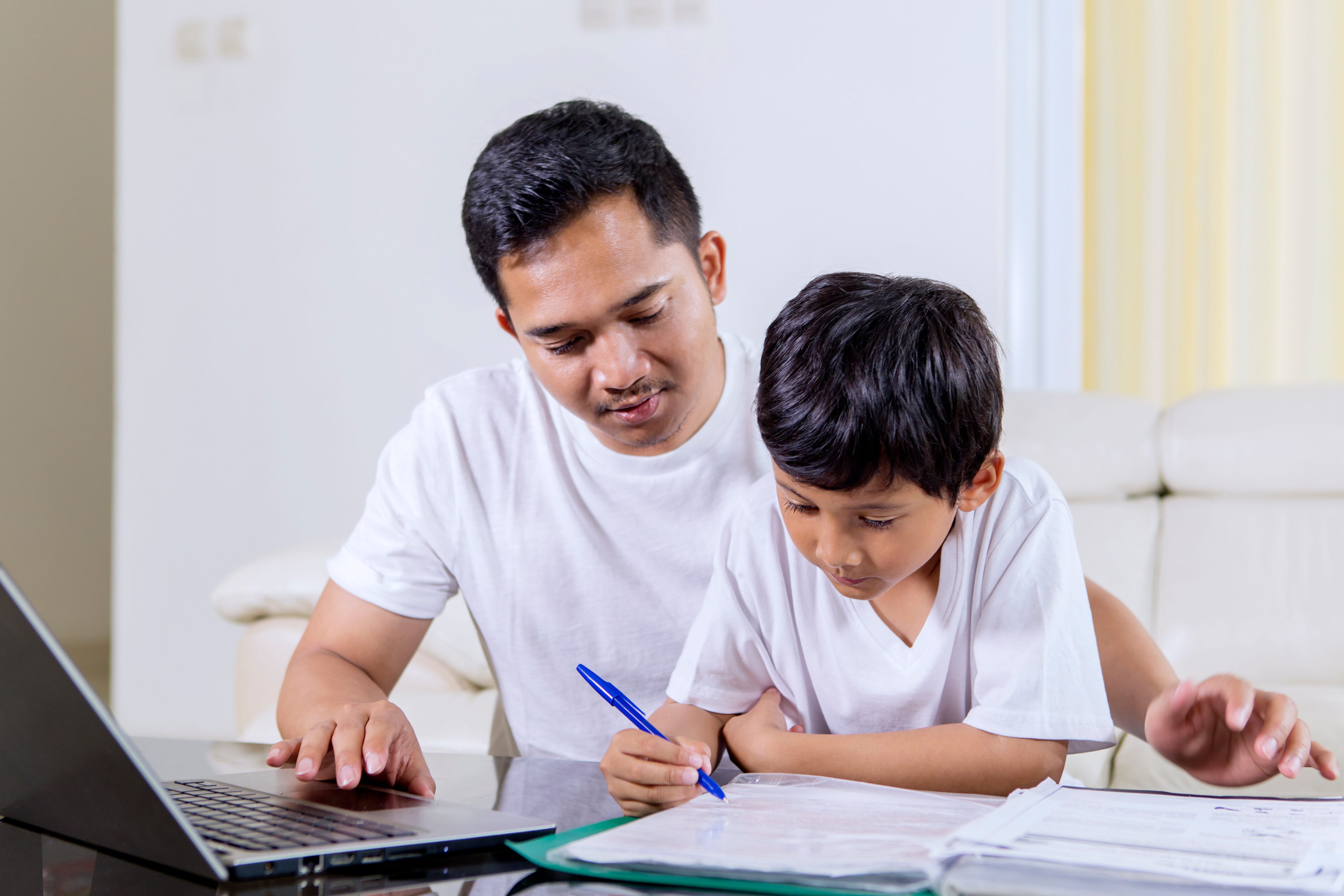 Little boy writing on textbook with his father. parent student resources